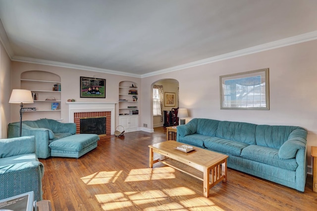 living room with arched walkways, built in shelves, a fireplace, wood finished floors, and crown molding