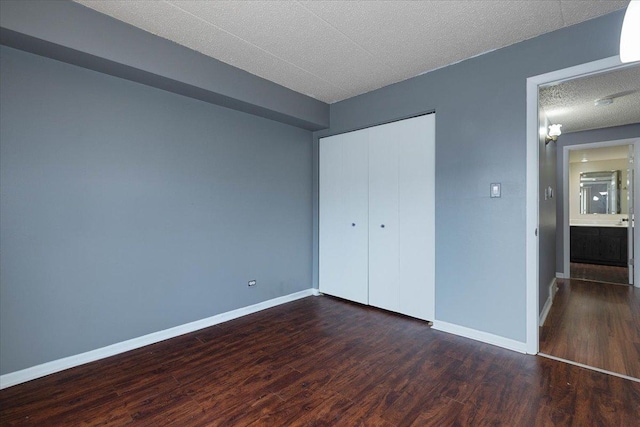 unfurnished bedroom featuring a textured ceiling, dark wood-style flooring, and baseboards