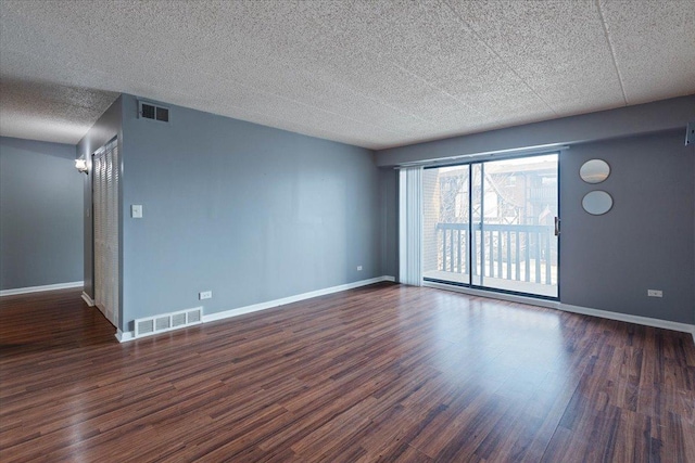 empty room featuring dark wood-style floors, visible vents, a textured ceiling, and baseboards