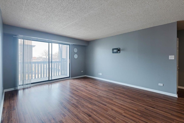 empty room with dark wood finished floors, a textured ceiling, and baseboards