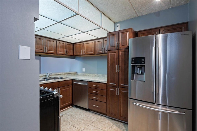 kitchen featuring light tile patterned floors, stainless steel appliances, a drop ceiling, and a sink