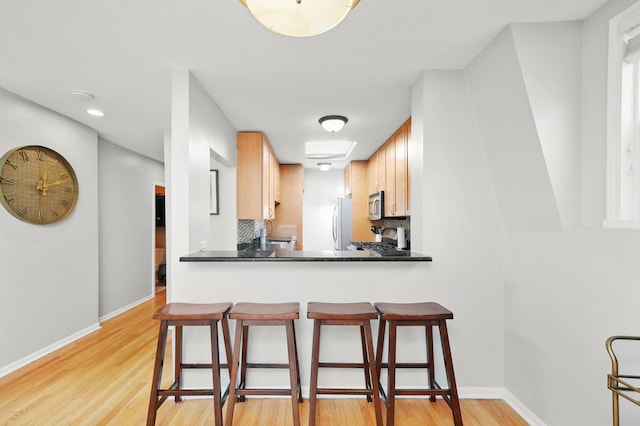 kitchen featuring a breakfast bar, backsplash, freestanding refrigerator, stainless steel microwave, and gas stove