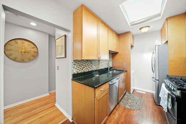 kitchen featuring a skylight, stainless steel appliances, backsplash, a sink, and light wood-type flooring