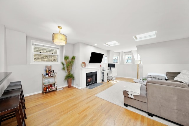 living area with vaulted ceiling with skylight, a fireplace with flush hearth, baseboards, and wood finished floors