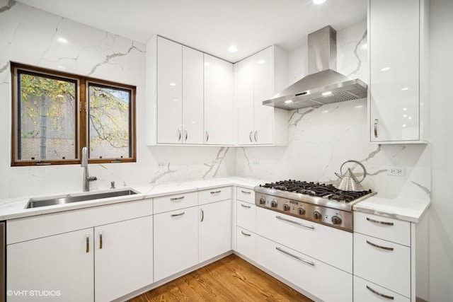 kitchen with light wood-style flooring, a sink, white cabinetry, wall chimney exhaust hood, and stainless steel gas stovetop