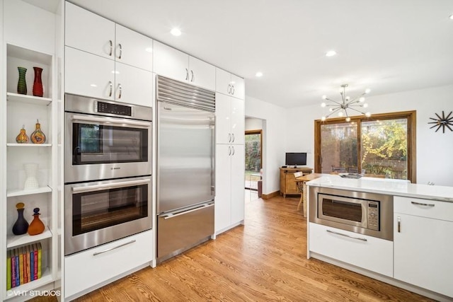 kitchen featuring built in appliances, a chandelier, white cabinetry, light countertops, and light wood-type flooring