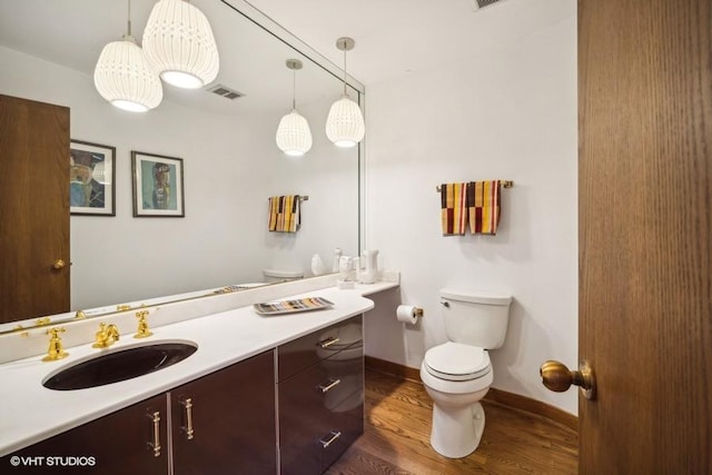 bathroom with visible vents, toilet, vanity, wood finished floors, and baseboards