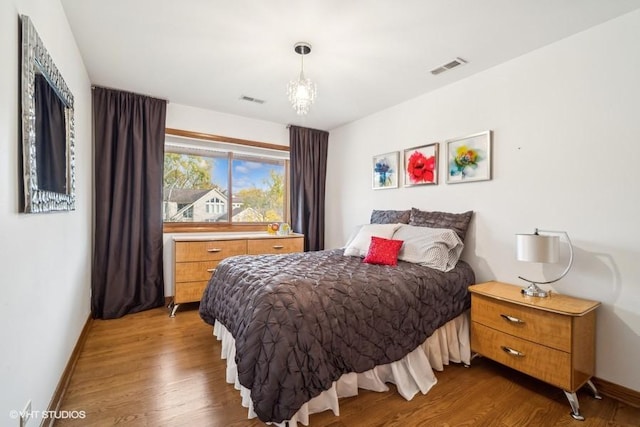 bedroom with baseboards, visible vents, and wood finished floors