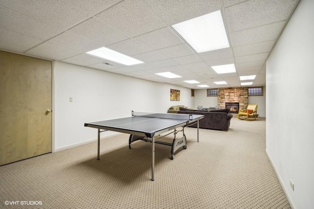 playroom featuring baseboards, a drop ceiling, a stone fireplace, and light colored carpet