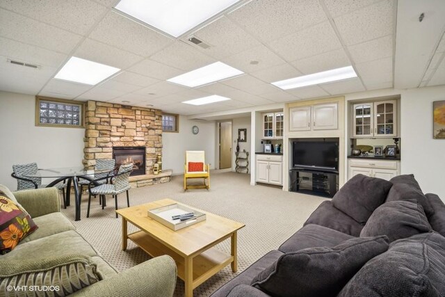 living room with light colored carpet, visible vents, a paneled ceiling, and a stone fireplace