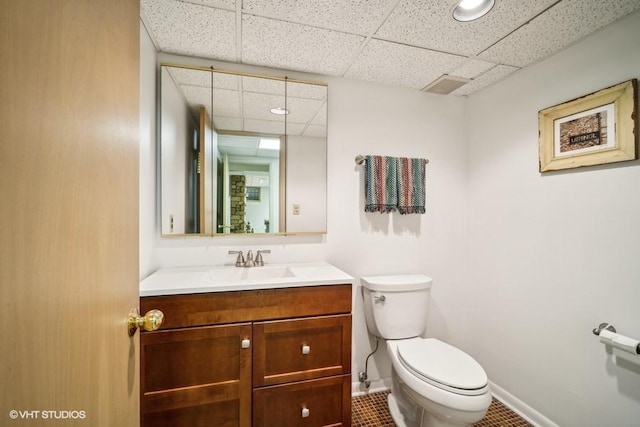 half bath with a paneled ceiling, vanity, toilet, and baseboards