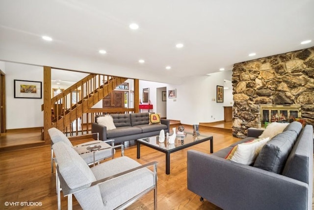 living room featuring a stone fireplace, recessed lighting, baseboards, stairway, and light wood finished floors