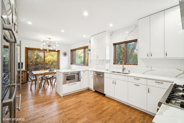 kitchen featuring a peninsula, a sink, light wood-style floors, appliances with stainless steel finishes, and tasteful backsplash