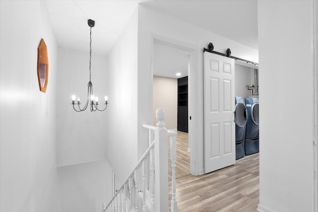 corridor featuring a barn door, an upstairs landing, washer and dryer, light wood finished floors, and an inviting chandelier