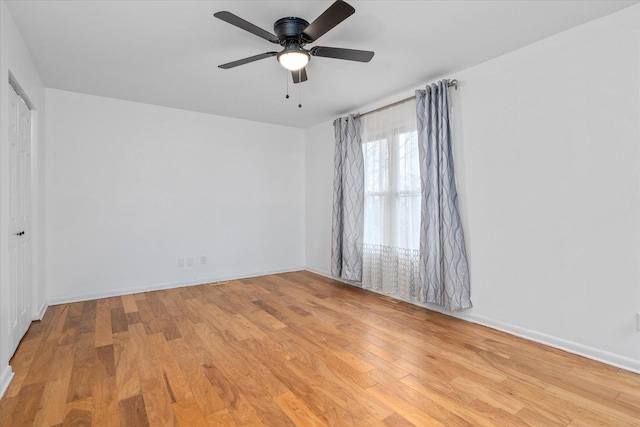 spare room with a ceiling fan, light wood-type flooring, and baseboards