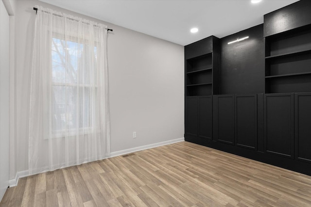 empty room with baseboards, visible vents, light wood-style floors, built in shelves, and recessed lighting