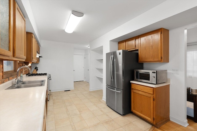 kitchen featuring brown cabinets, stainless steel appliances, light countertops, and a sink