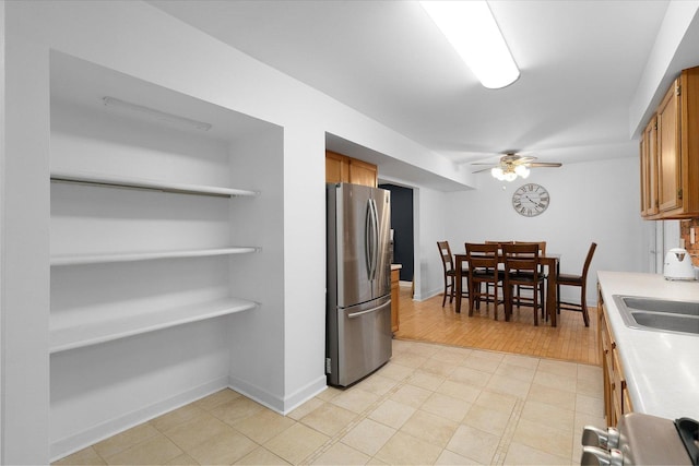 kitchen featuring ceiling fan, a sink, light countertops, freestanding refrigerator, and brown cabinets