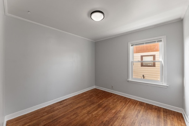 empty room featuring wood-type flooring, baseboards, and crown molding