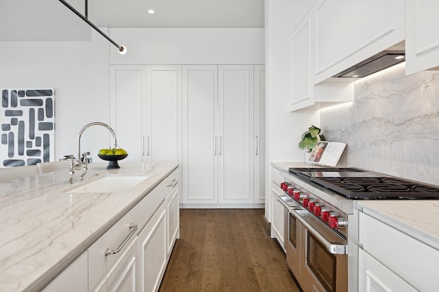 kitchen with range with two ovens, dark wood-type flooring, a sink, white cabinetry, and light stone countertops