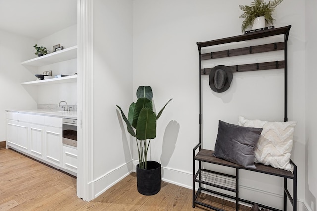 interior space with light wood-type flooring, a sink, stainless steel oven, and baseboards