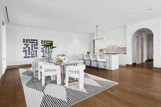 dining area featuring baseboards, arched walkways, dark wood finished floors, and recessed lighting