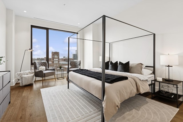 bedroom featuring recessed lighting, a city view, dark wood finished floors, and baseboards