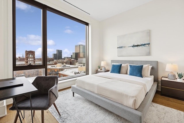 bedroom featuring multiple windows, light wood-style flooring, and a city view