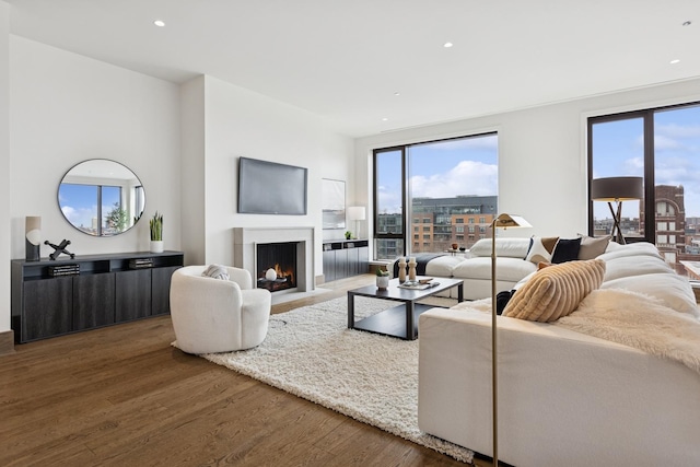 living room featuring dark wood-type flooring, a wealth of natural light, a warm lit fireplace, and recessed lighting