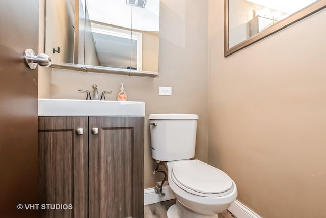 half bathroom featuring visible vents, baseboards, toilet, wood finished floors, and vanity