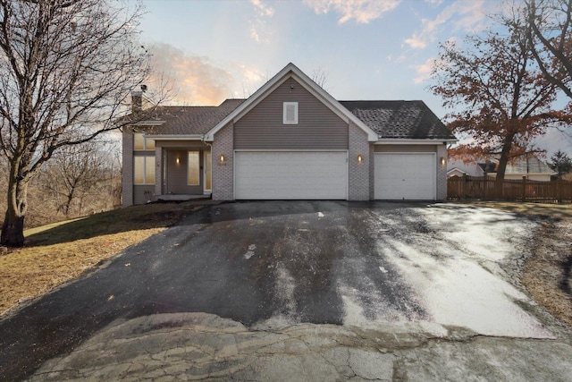 view of front of house with driveway, brick siding, an attached garage, and fence