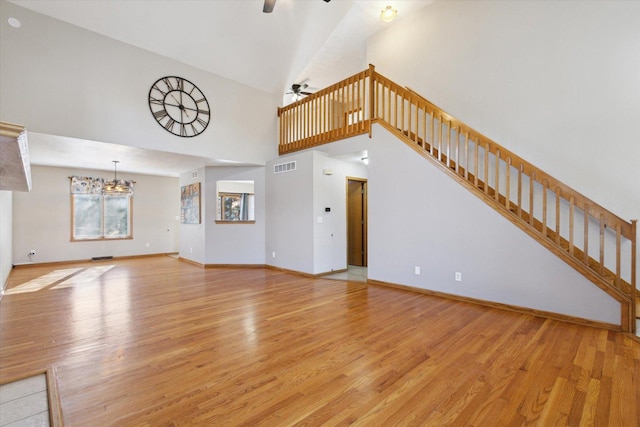 unfurnished living room with baseboards, visible vents, stairs, light wood-type flooring, and ceiling fan with notable chandelier