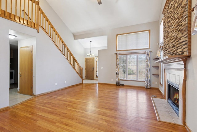 unfurnished living room with light wood-style flooring, an inviting chandelier, a high ceiling, stairs, and a fireplace