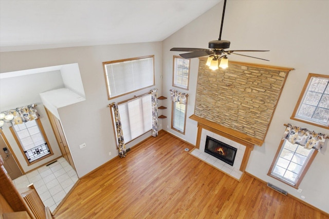 unfurnished living room with high vaulted ceiling, light wood finished floors, visible vents, and a tiled fireplace