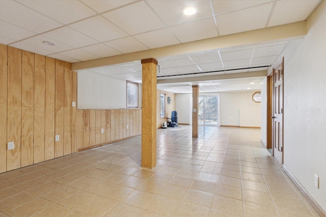 basement with light tile patterned floors, wooden walls, and a drop ceiling