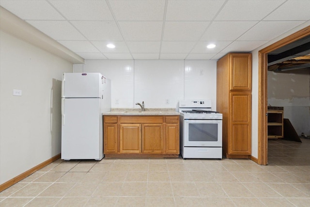 kitchen with white appliances, light tile patterned floors, baseboards, brown cabinetry, and a sink