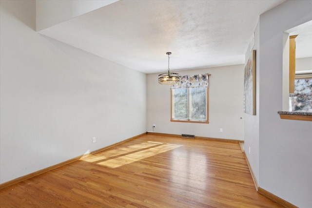 empty room featuring a textured ceiling, wood finished floors, visible vents, and baseboards