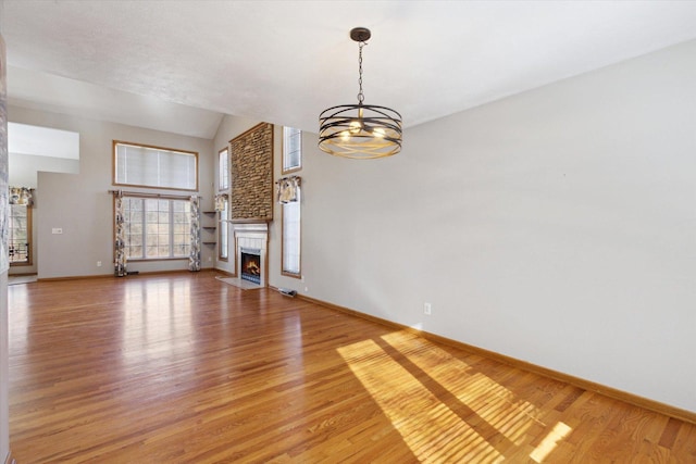 unfurnished living room featuring a notable chandelier, light wood-style flooring, a fireplace with flush hearth, high vaulted ceiling, and baseboards