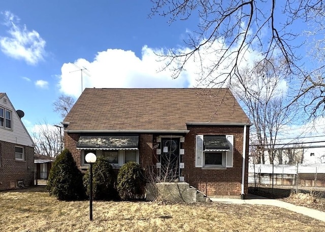 view of front of property featuring a shingled roof, brick siding, and fence