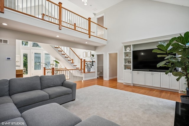 living area featuring light wood finished floors, stairway, a high ceiling, and visible vents