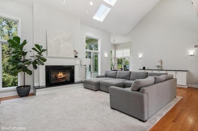 living room featuring a skylight, visible vents, a glass covered fireplace, wood finished floors, and high vaulted ceiling