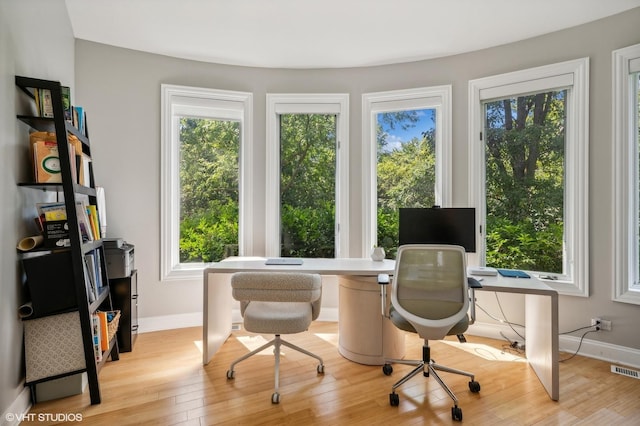 office area featuring baseboards, light wood-type flooring, visible vents, and a healthy amount of sunlight