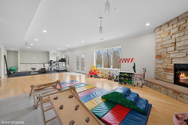 game room featuring a stone fireplace, french doors, wood finished floors, and crown molding