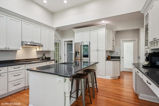 kitchen featuring dark countertops, a kitchen breakfast bar, stainless steel appliances, under cabinet range hood, and a sink