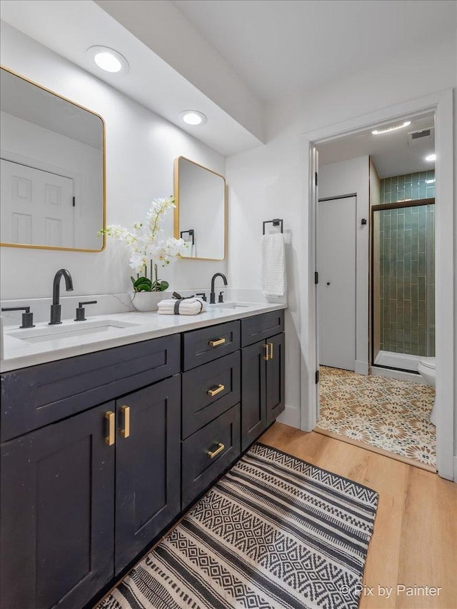 full bathroom featuring double vanity, wood finished floors, a stall shower, and a sink