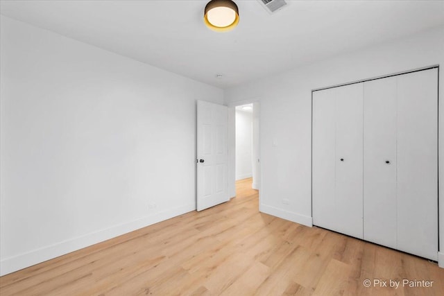 unfurnished bedroom featuring light wood finished floors, a closet, visible vents, and baseboards