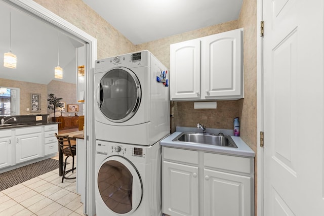 laundry room featuring a sink, stacked washing maching and dryer, light tile patterned floors, and wallpapered walls