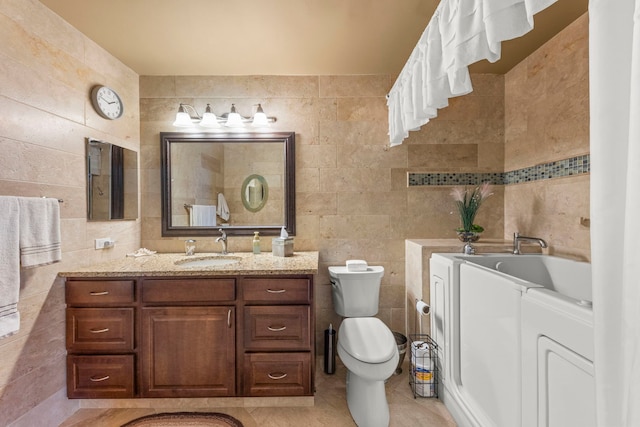 bathroom with tile walls, toilet, vanity, independent washer and dryer, and a bath