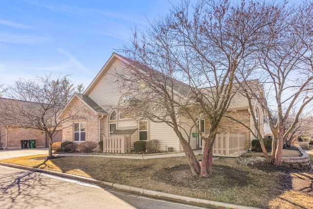 view of front of home with driveway, brick siding, and fence