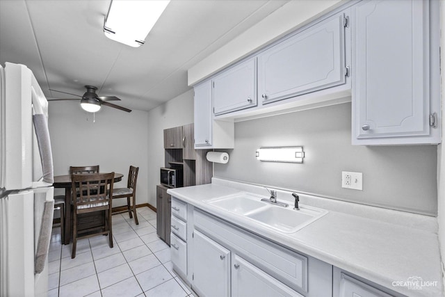 kitchen with light tile patterned floors, freestanding refrigerator, ceiling fan, a sink, and light countertops